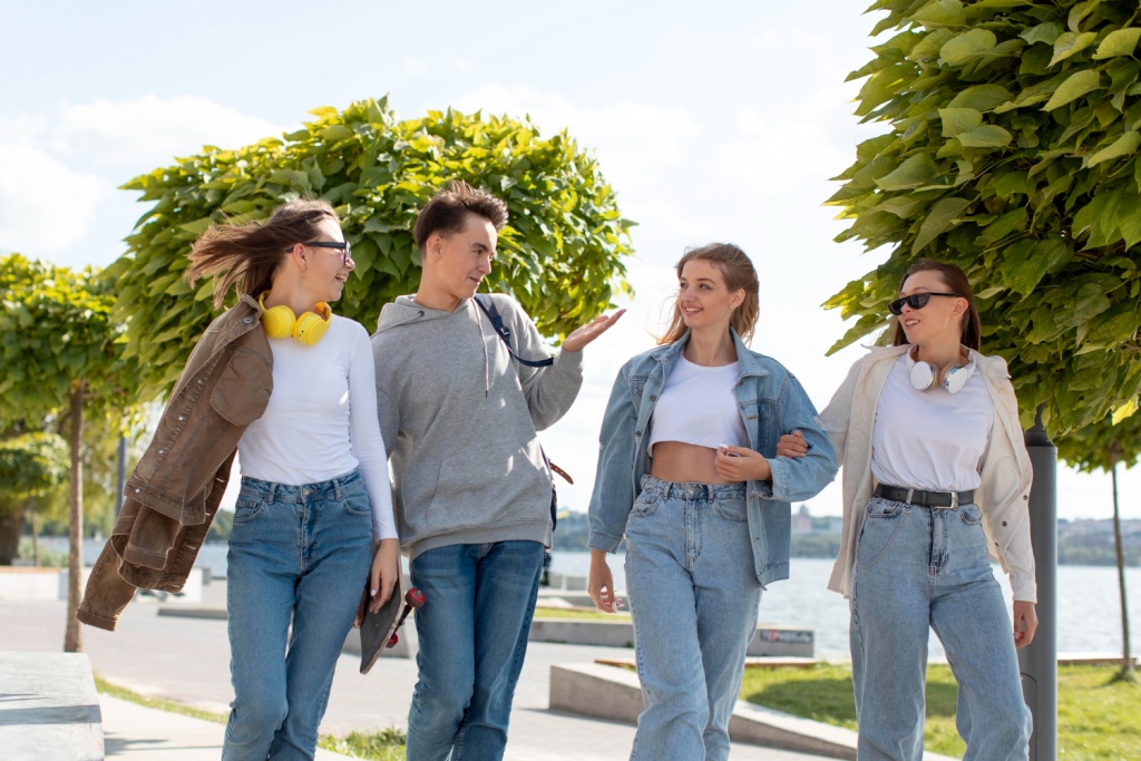 Four friends walking and talking together on a sunny waterfront promenade beside calm water