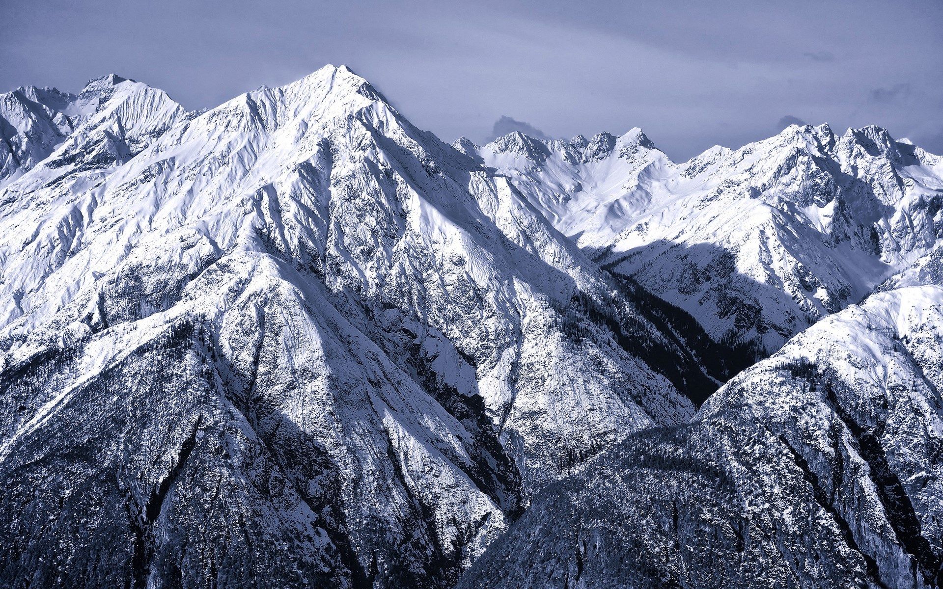 Snow-covered jagged mountain peaks and steep ridges under a pale overcast sky